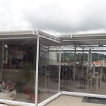 Cobertura de Telha Sanduiche, pintada em branca, com estrutura em aço galvanizado e pin com fechamentos com cortinas rolô, de visor e bordas brancas.
